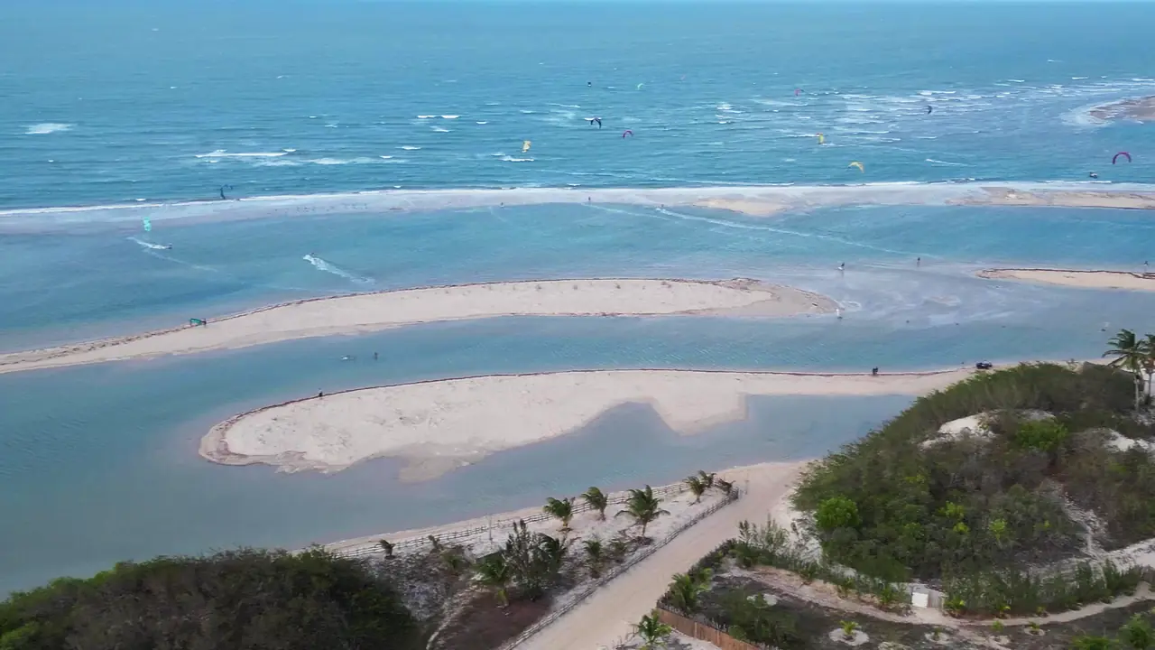 Banco de areia em forma de meia-lua na lagoa de água plana de Tatajuba, com kites velejando no mar ao fundo
