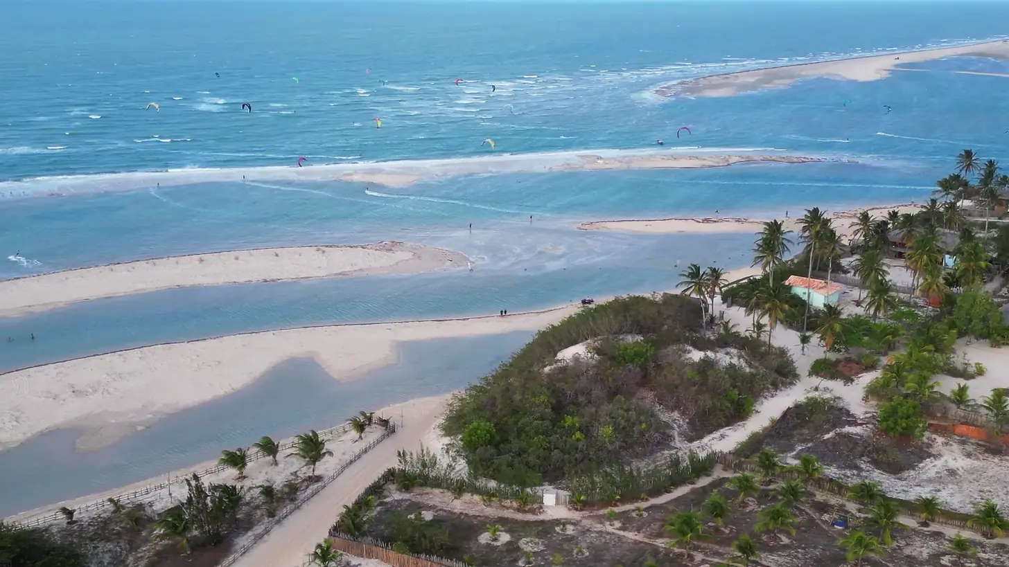 Vista aérea de Tatajuba, no Ceará, com bancos de areia, lagoa de água plana e kites velejando no mar ao fundo