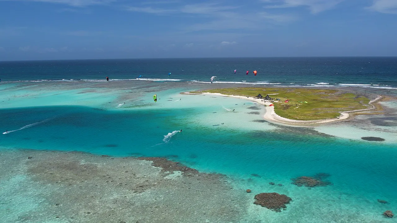 Vista aérea ampla do atol de Los Roques com recifes, bancos de areia e lagoas de tons de azul e verde