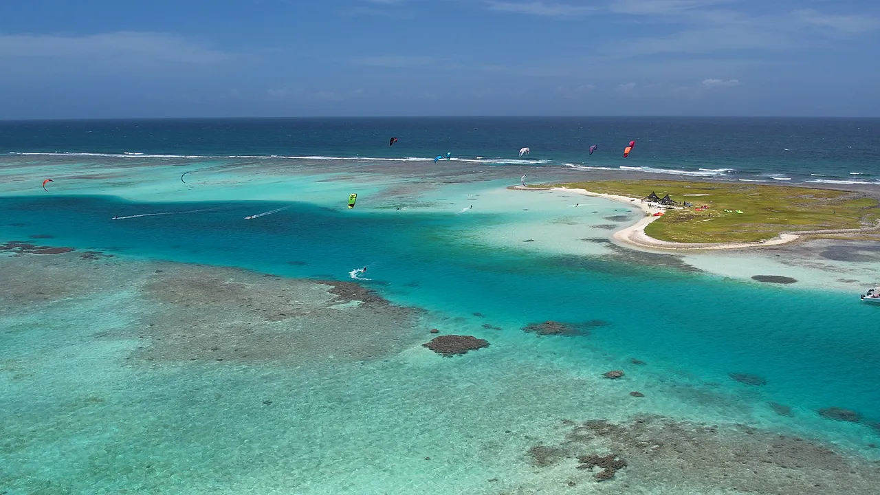 Banco de areia e lagoa de água turquesa em Los Roques vistos do alto, com kitesurfistas velejando ao longe