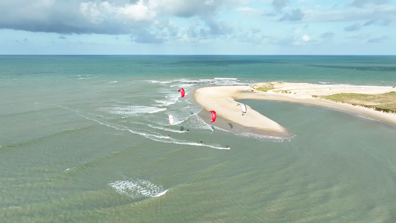 Velejadores de kitesurf em um banco de areia em Maracajaú, Rio Grande do Norte, com céu azul e água esverdeada