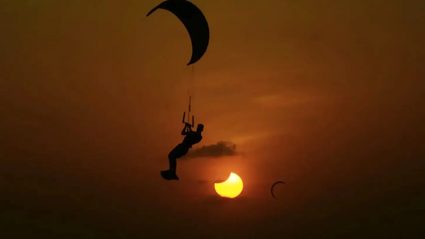 Kitesurfista saltando recortado contra o pôr do sol alaranjado, com a silhueta do kite e o sol ao fundo, em Barra Grande, no Piauí
