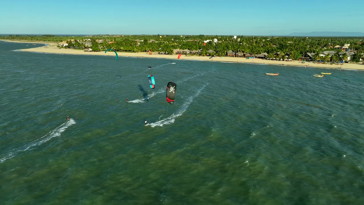 Kitesurfistas velejando em mar verde com um banco de areia ao fundo, em Barra Grande, no Piauí