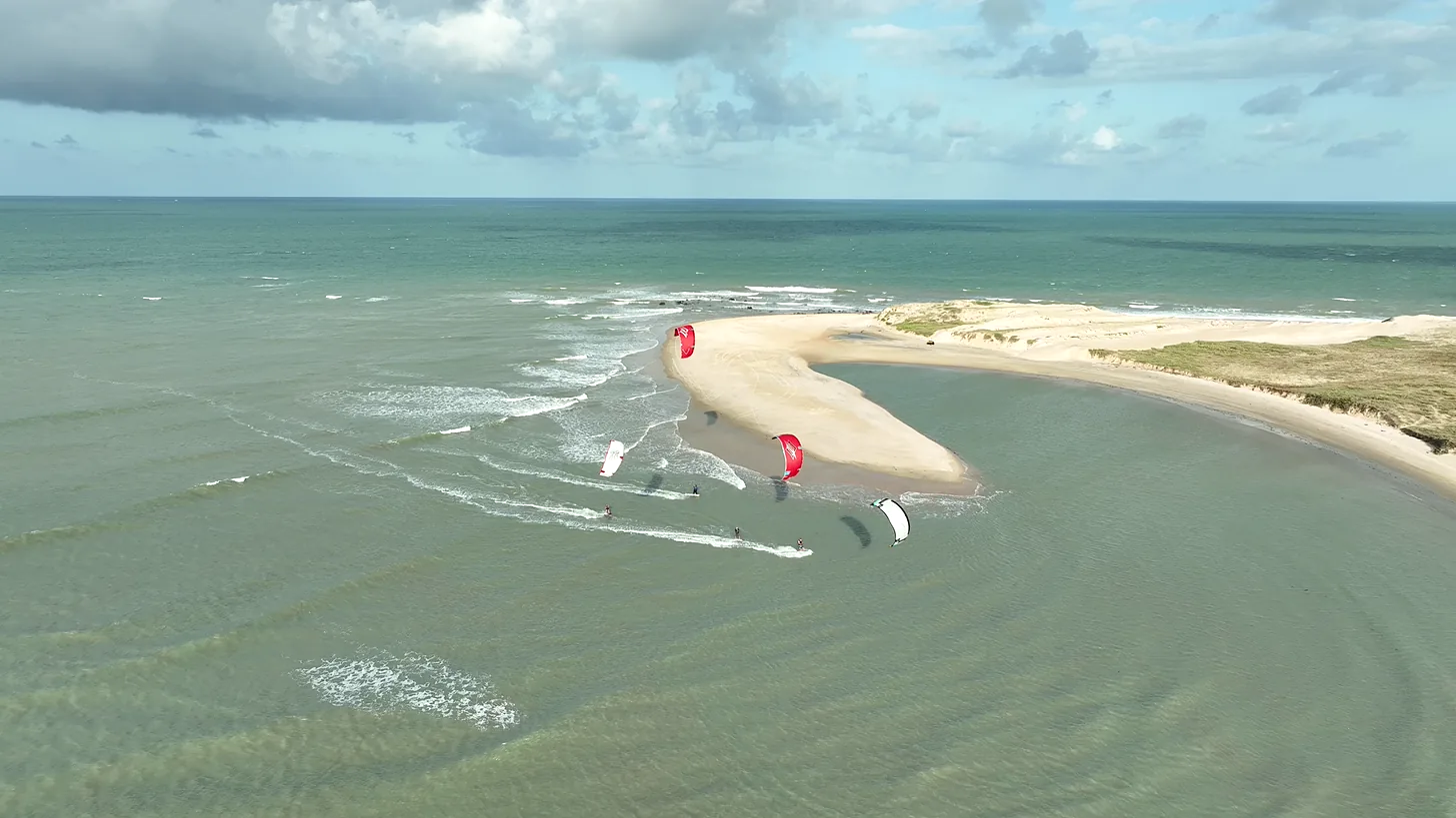 Vista aérea de Maracajaú, no Rio Grande do Norte, com kitesurfistas velejando na água rasa e morna ao lado de um banco de areia